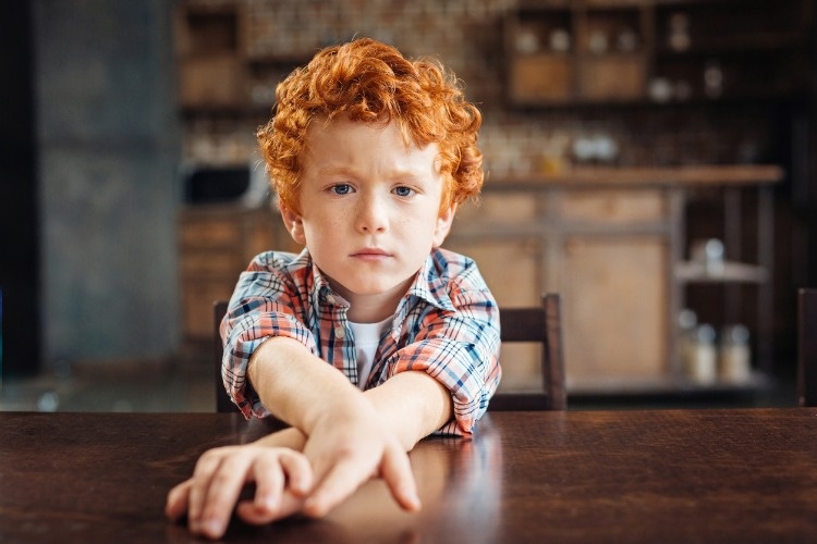 bored-redhead-little-boy-sitting-at-table-picture-id849818142_01