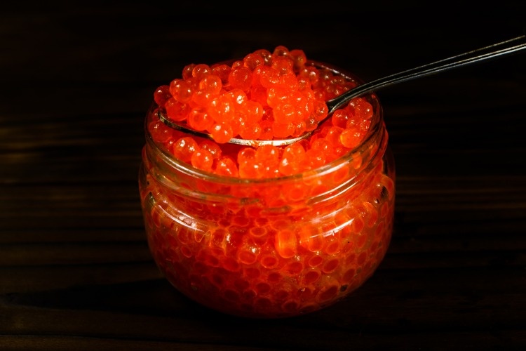 red-caviar-in-a-spoon-above-the-glass-jar-picture-id901066948