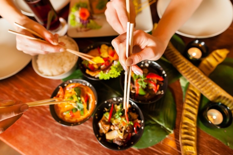 bowls-of-food-in-thai-restaurant-and-hands-using-chopsticks-picture-id471444155