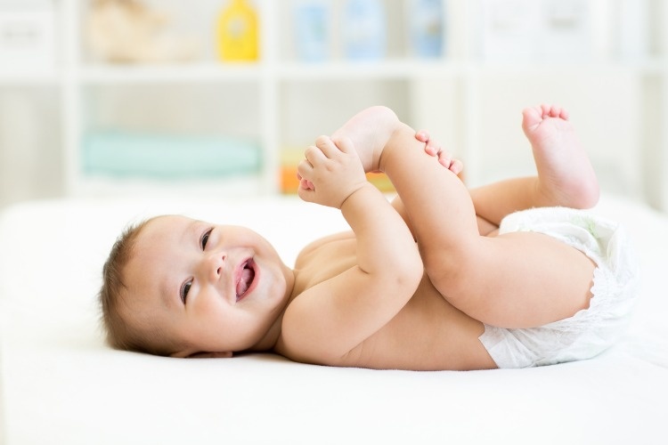baby-lying-on-white-bed-and-holding-legs-picture-id537424238